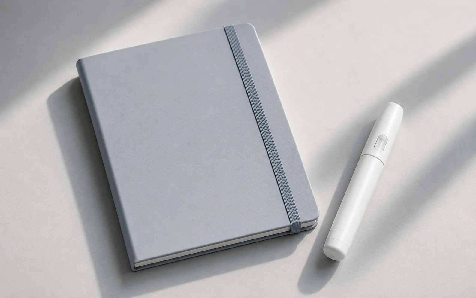 A plain unbranded medical injector pen and a blank notebook on a calm neutral clinical surface