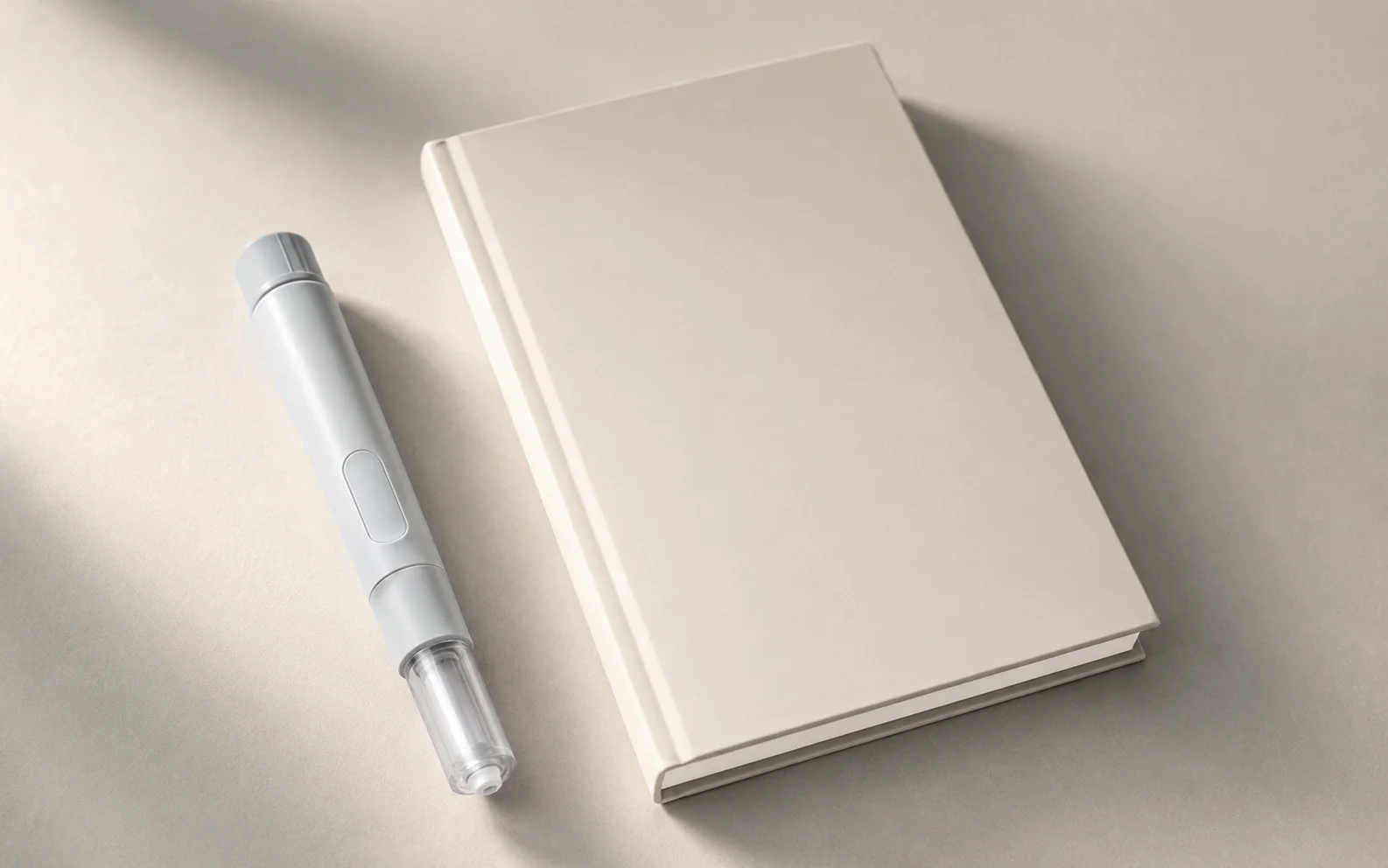 A plain unbranded medical injector pen beside a blank notebook on a calm neutral clinical surface