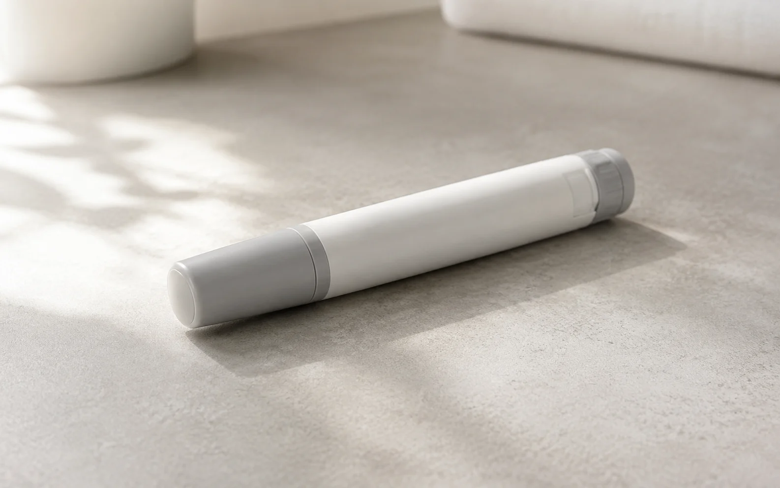 A plain unbranded medical injector pen resting on a calm neutral surface with soft light