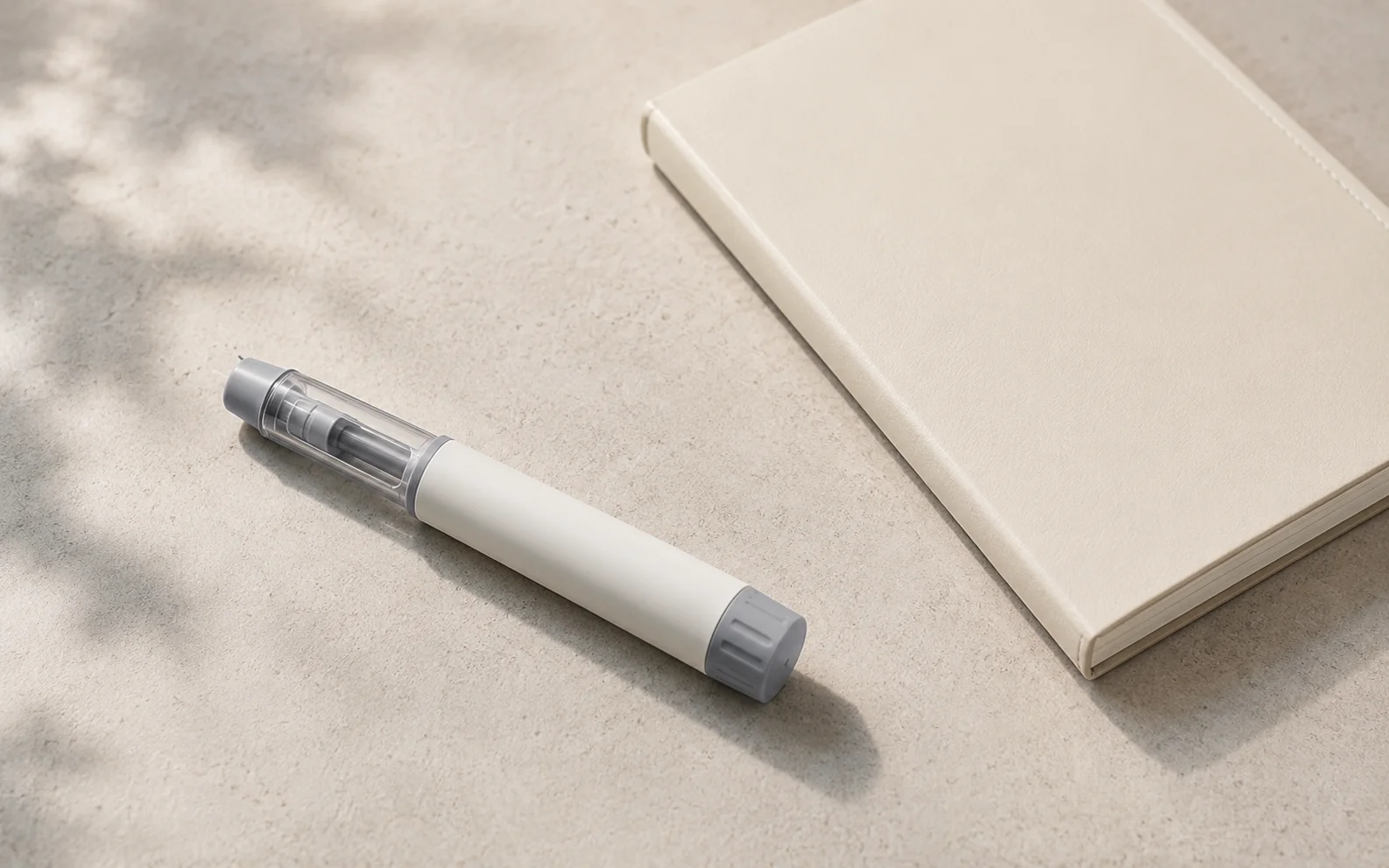 A plain unbranded medical injector pen on a clean neutral surface beside a simple notebook