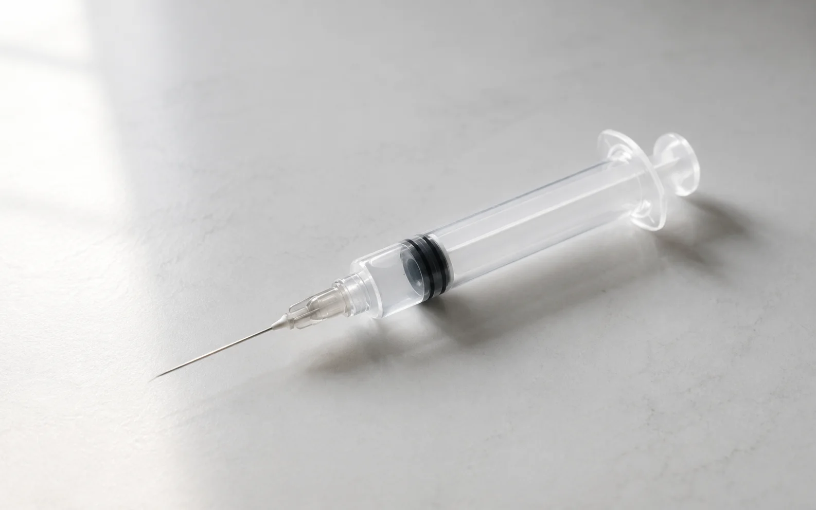 A single medical syringe with a fine needle resting on a clean clinical surface