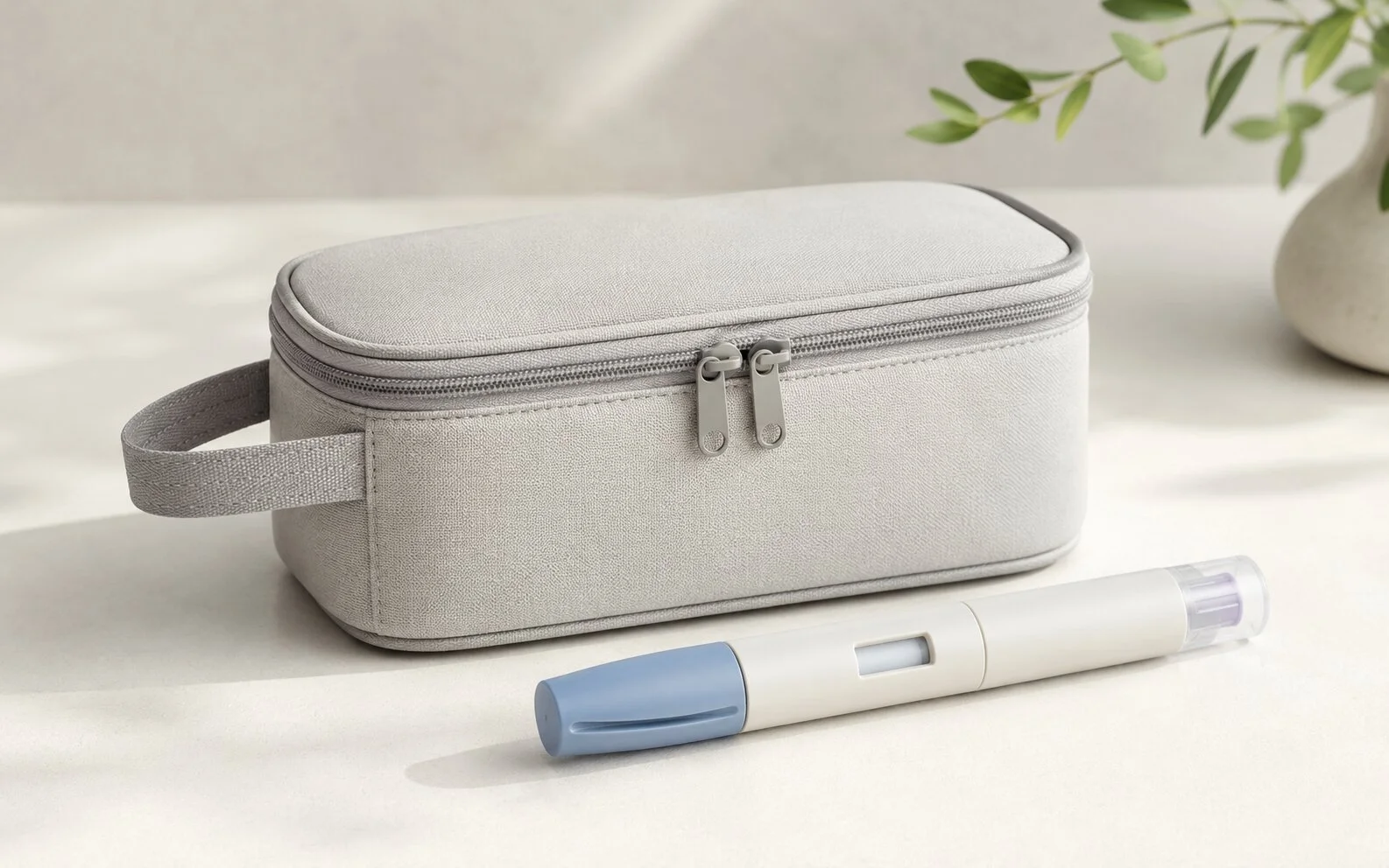 A plain unbranded insulated travel pouch beside a generic medical injector pen on a calm neutral surface