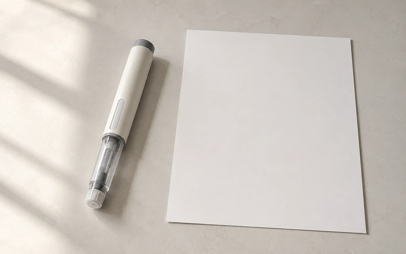 A plain unbranded medical injector pen beside a blank document on a calm neutral surface