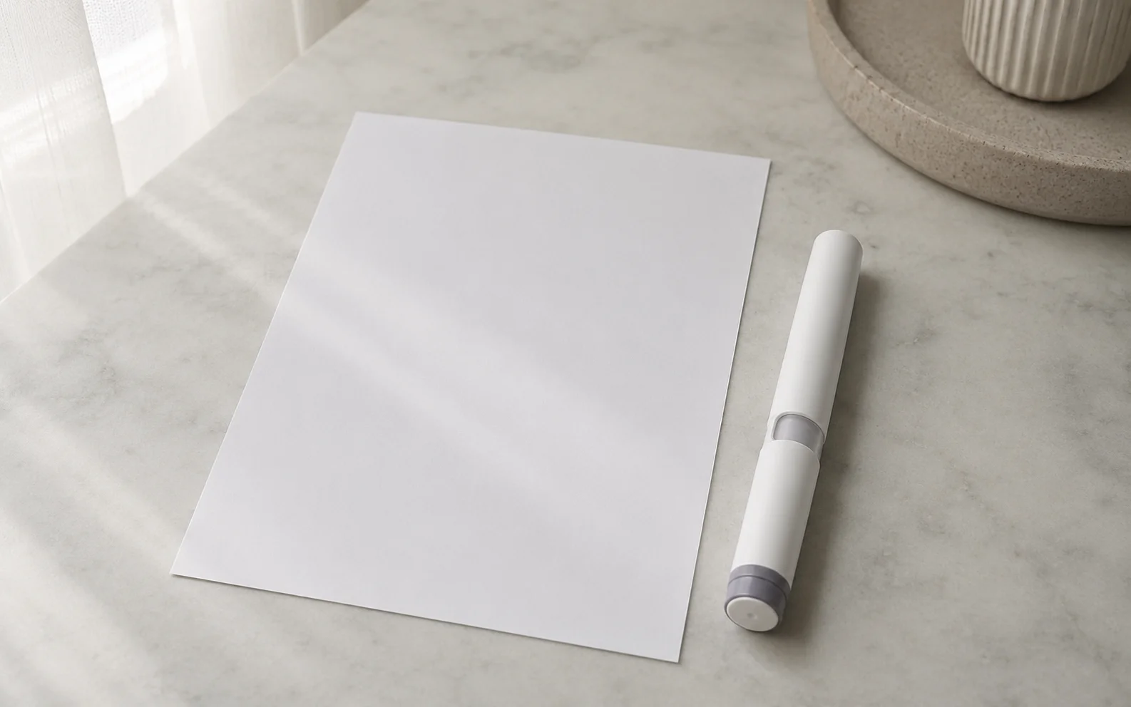 A plain unbranded medical injector pen resting on a calm neutral surface beside a blank document