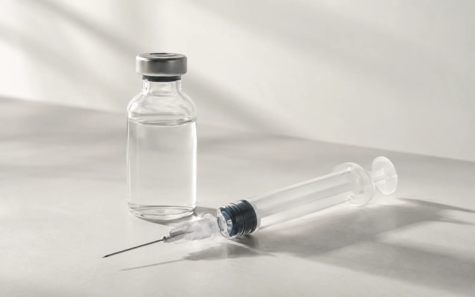 A plain unmarked medication vial and syringe on a clean neutral clinical surface