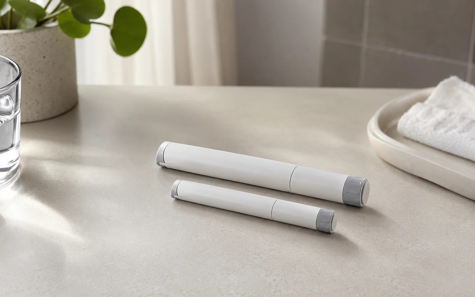 Two plain unbranded medical injector pens of slightly different sizes on a clean clinical surface