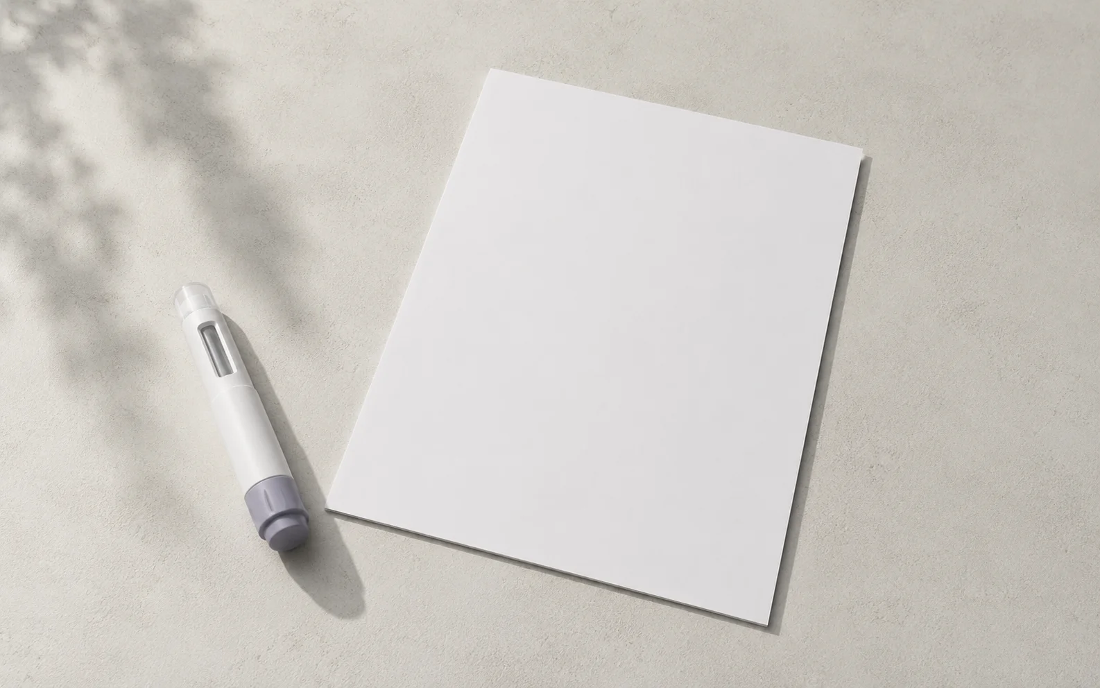 A plain unbranded medical injector pen beside a blank document on a calm neutral surface