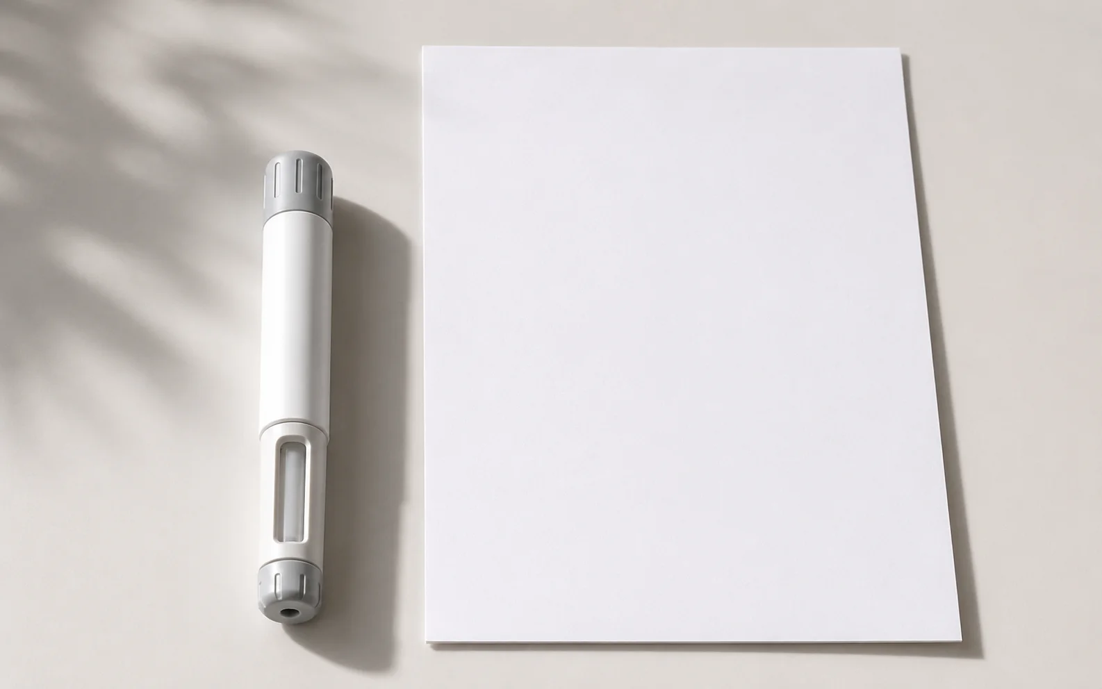 A plain unbranded injector pen beside a blank document on a calm neutral surface