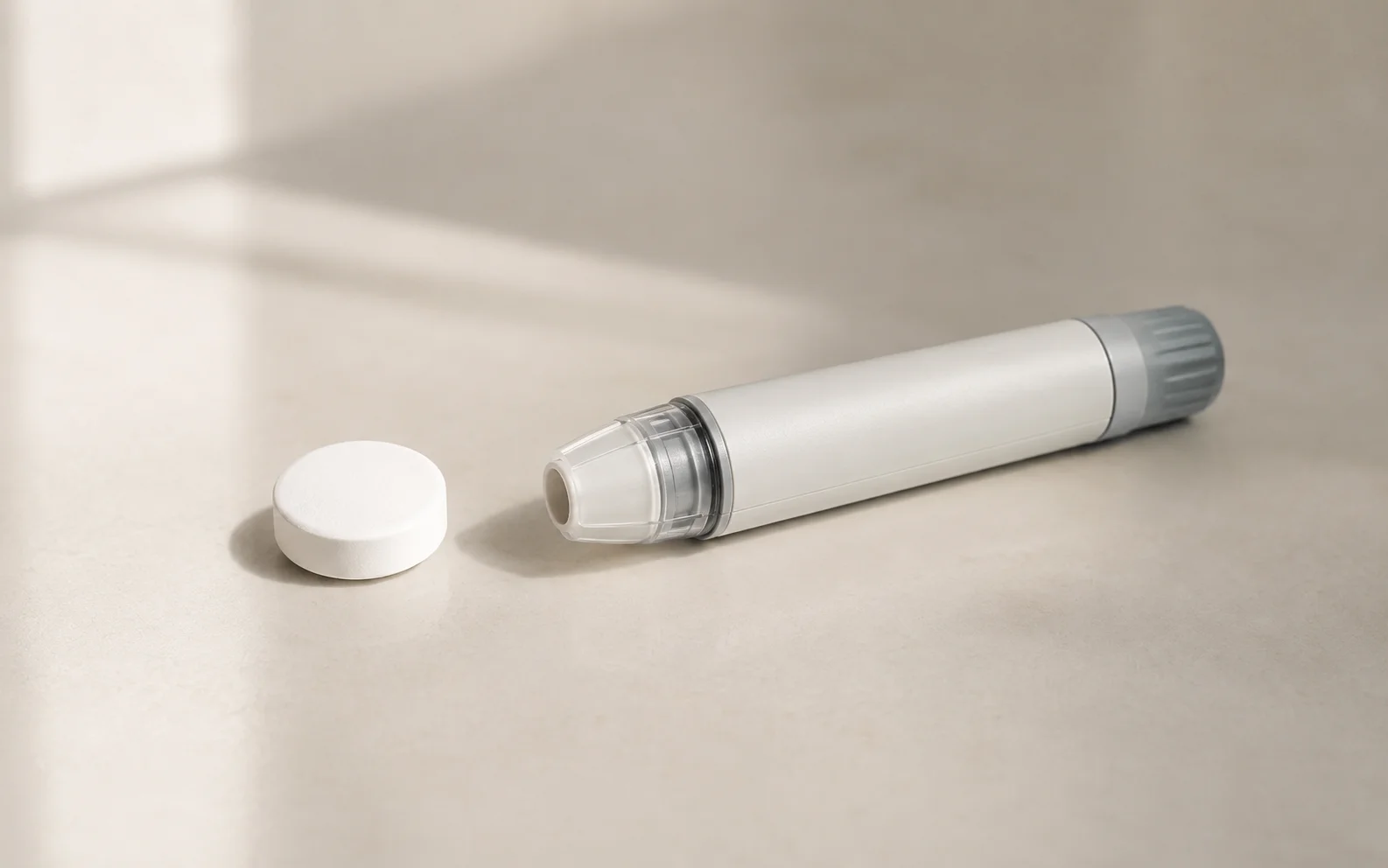 A plain unbranded tablet and a plain unbranded injector pen side by side on a calm neutral surface