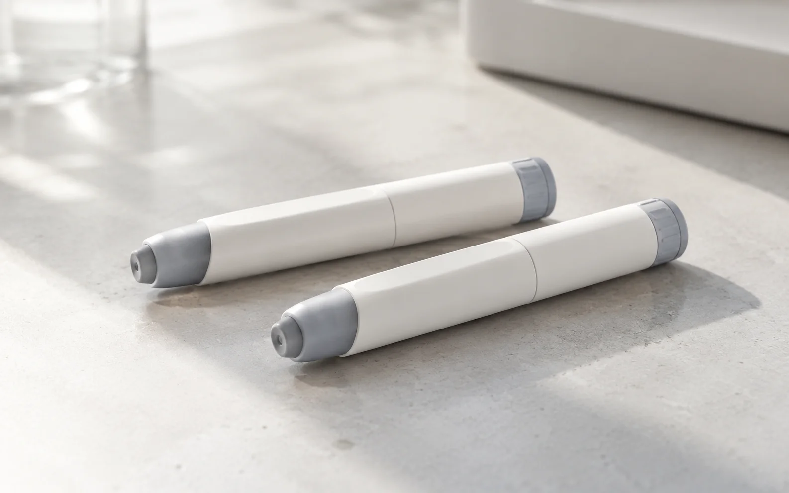 Two plain unbranded medical injector pens on a clean clinical surface