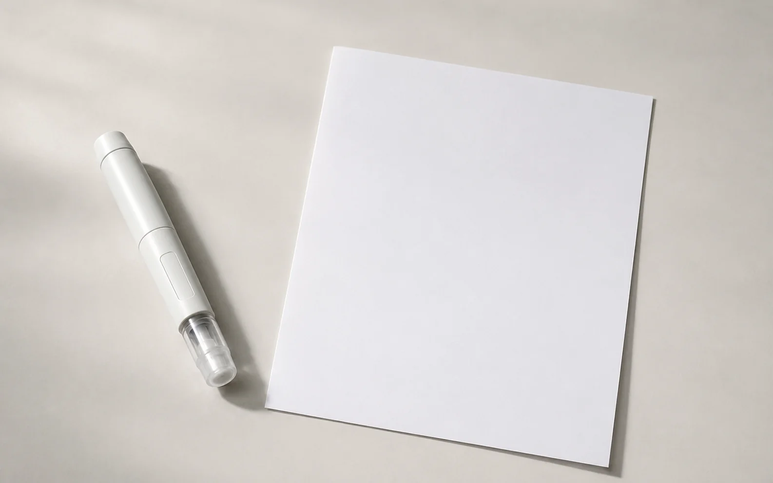 A plain unbranded medical injector pen beside a blank chart on a calm neutral surface