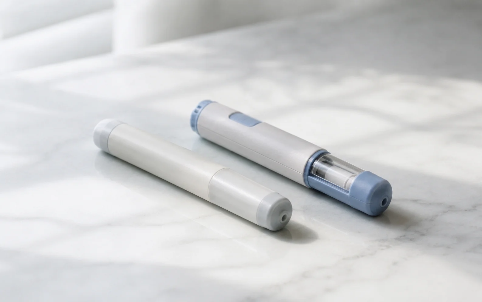 Two plain unbranded medical injector pens on a clean clinical surface