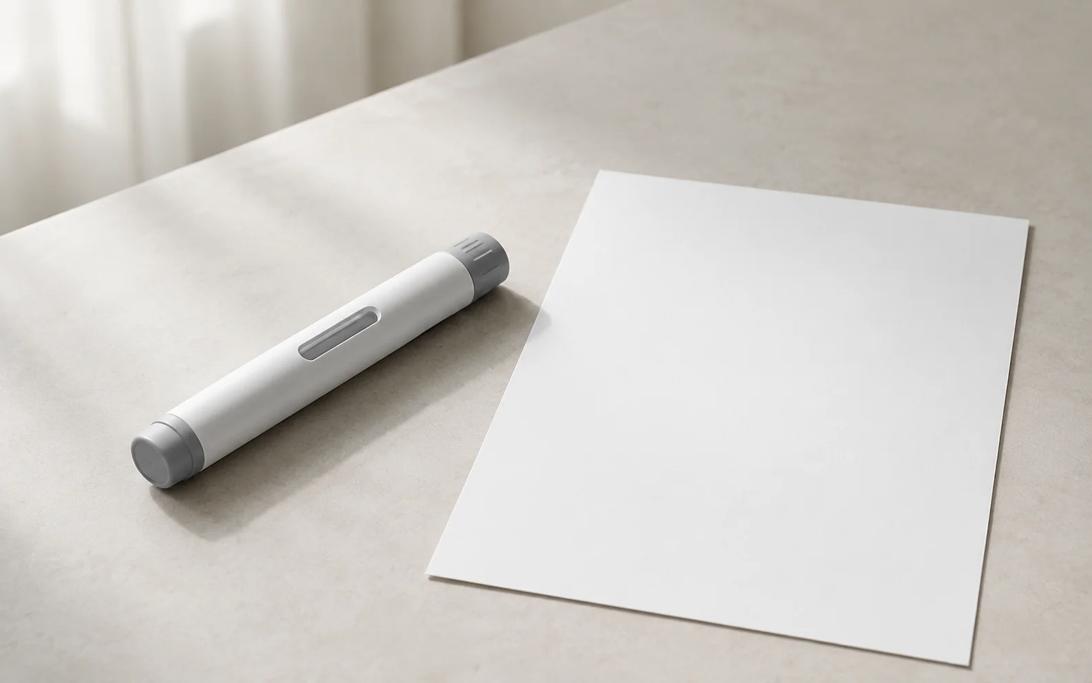 A plain unbranded medical injector pen resting on a calm neutral surface beside a blank document
