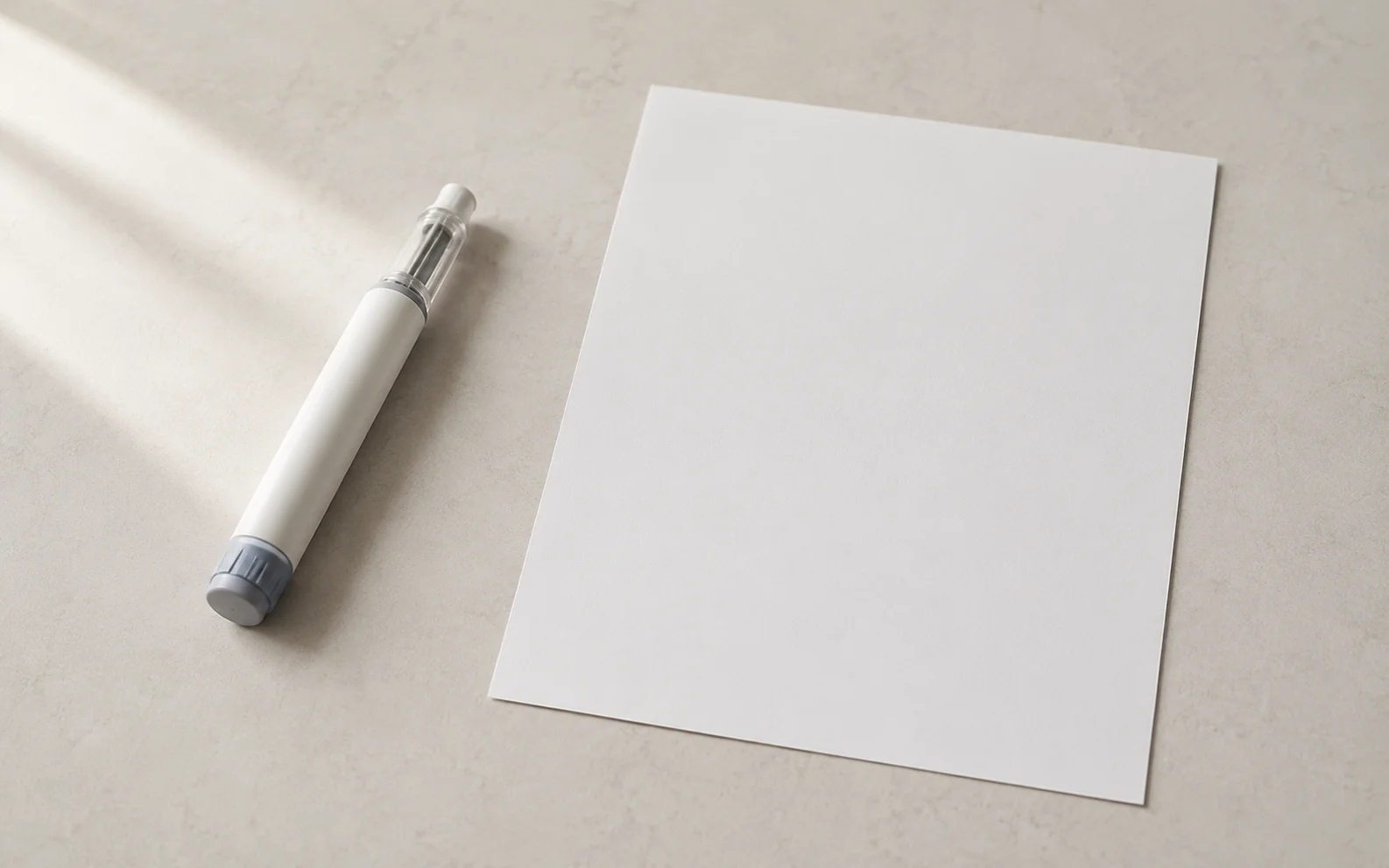 A plain unbranded medical injector pen beside a blank chart on a calm neutral surface